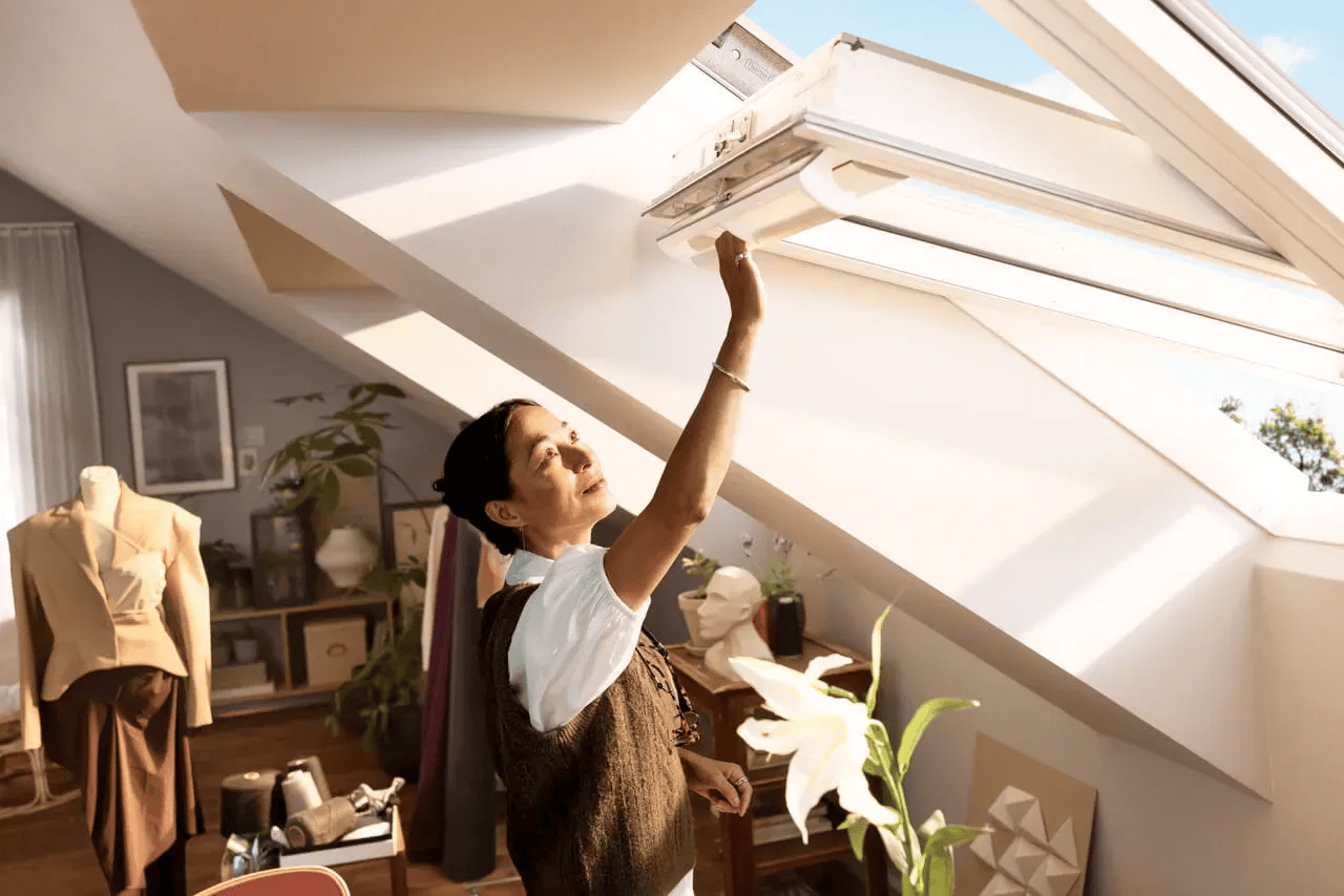 Vrouw opent een VELUX dakvenster op een lichte zolder — dakvensters bij Bouwcenter MVR in Oostende